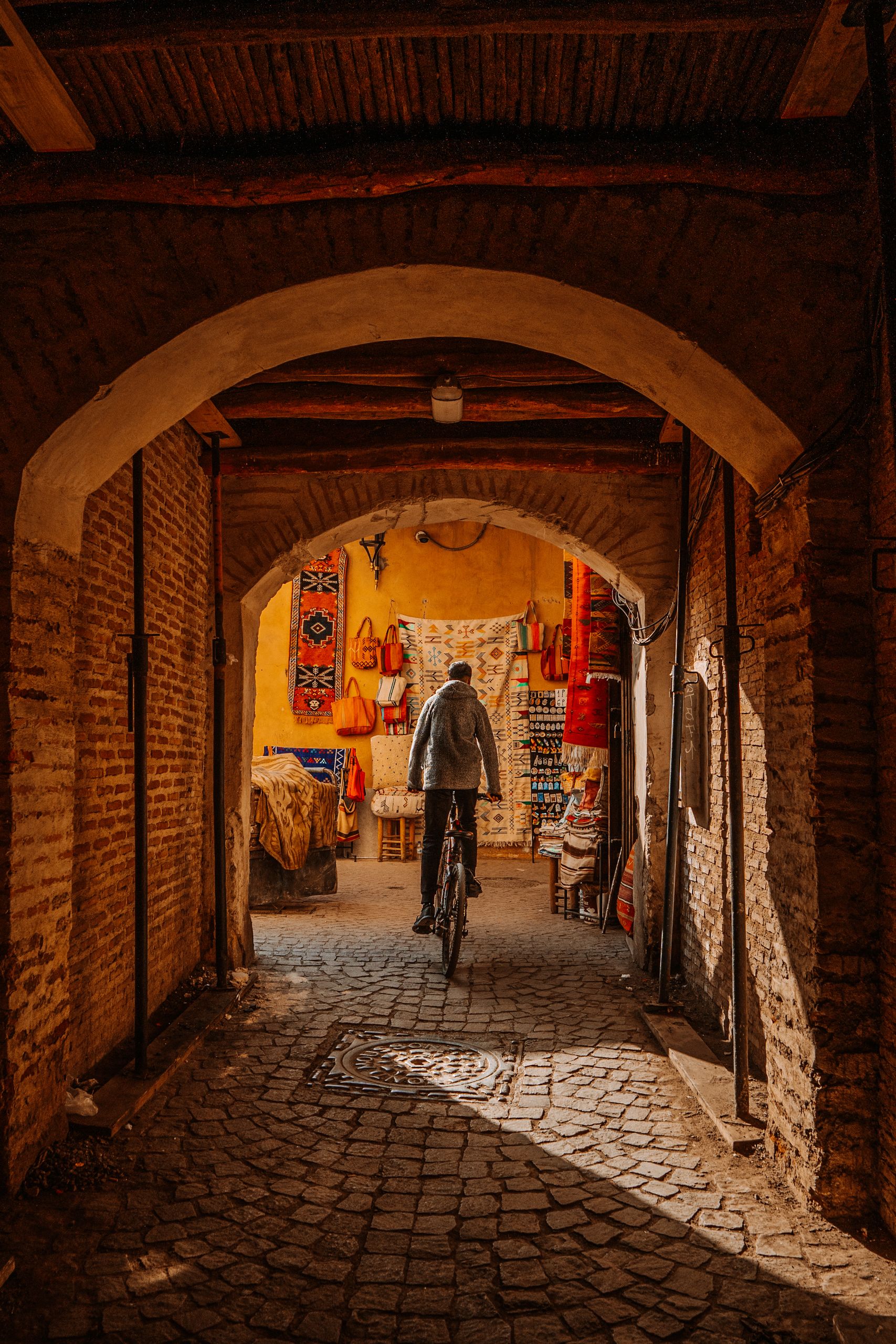 A cyclist travels through the narrow archway in Marrakesh Medina, showcasing vibrant market colors.